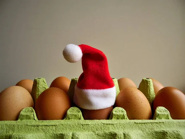 Santa\'s hat on an egg, white and brown eggs in a tray and Santa\'s hat on one of the eggs, Christmas theme