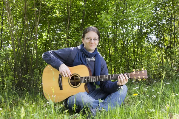 Young man playing guitar outdoors in green fields — Stock Photo, Image