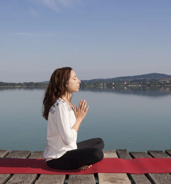 Young caucasian woman meditating on a summer day by a lake on a — Stock Photo, Image