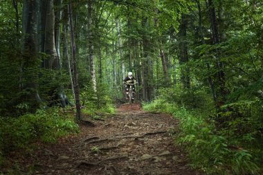 Man, cyclist in full face helmet on the yellow enduro bicycle jumping in a green forest. Summer time, Ukraine
