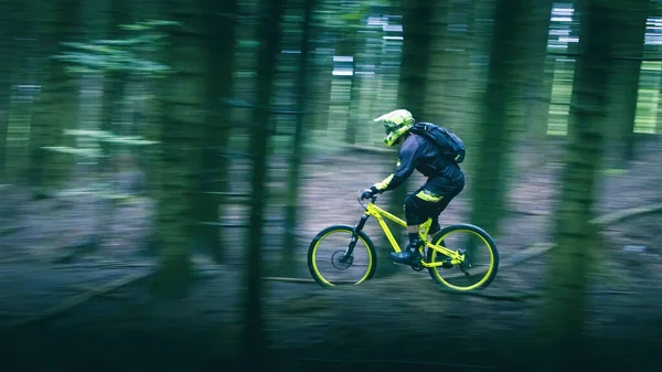 Man in full face helmet on the yellow enduro bicycle with backpack very fast rides in the forest. Trees was blurred high speed. Summer time, Ukraine