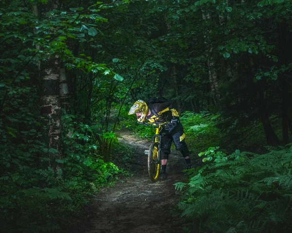 Man, cyclist in the full face helmet stands with the yellow enduro bicycle in the green forest. Summer time, Ukraine