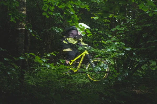 Man, cyclist in the full face helmet fast rides on the yellow enduro bicycle in the green forest Ukraine