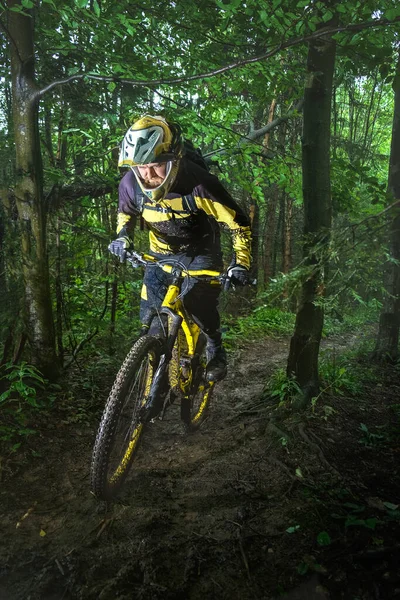 Man, cyclist in the full face helmet uphill on the yellow enduro bicycle in the green forest Ukraine
