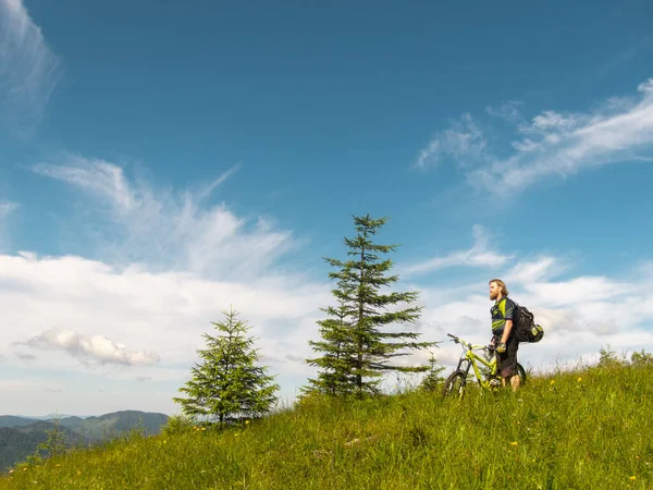 A man with a beard and long hair, a cyclist, stands with the yellow enduro bicycle against the blue sky, Ukraine