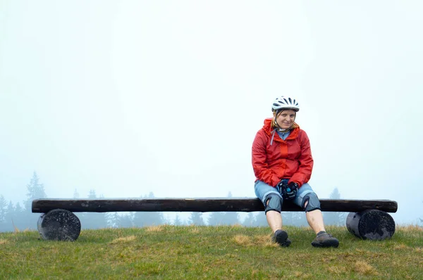 A young girl in a red jacket and bicycle helmet sits on a bench, Ukraine