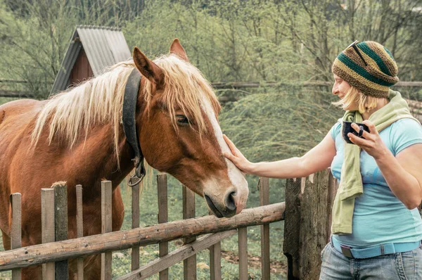 A young girl in a hat with a cup of tea stroking a horse, Ukraine