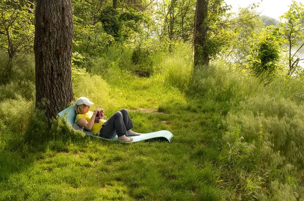 A young girl is lying in the woods on a wiggle mat and knitting with needles, Ukraine