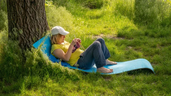 A young girl is lying in the woods on a wiggle mat and knitting with needles, Ukraine