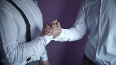 Damat ve beyaz gömlekli damadın arkadaşı el sıkışmadan hemen sonra birbirlerine sarılırlar. Kapat.