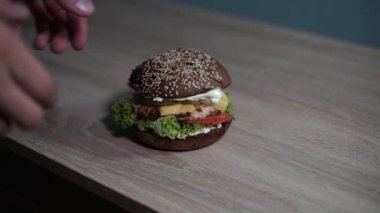 Erkek eli, ahşap bir masadan lezzetli, sulu bir burger alıyor.