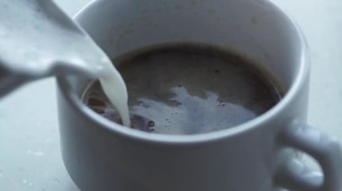 Süt ve köpüğün döküldüğü beyaz bir fincan yakın plan kahve. Adam kapuçino yapar, kahve fincanına süt döker.
