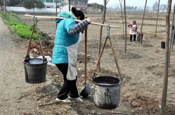 China: Mujer llevando cubos de agua repartidos desde el yugo de hombro — Foto de Stock