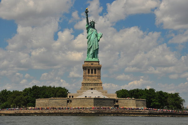 NYC: The Statue of Liberty standing above its base with crowds of tourists visiting the island on a Summer afternoon x