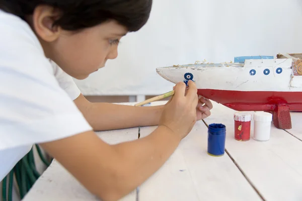 Boy painting and renovating old wooden boat — Stock Photo, Image