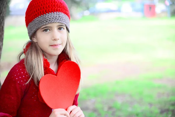 Hermosa chica con sombrero de ganchillo rojo sosteniendo gran corazón de fieltro San Valentín — Foto de Stock