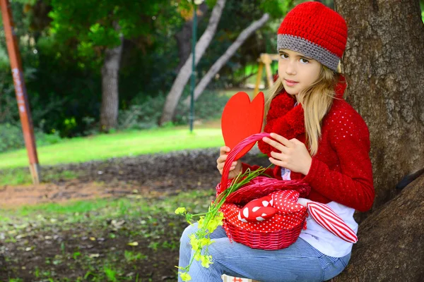 Menina bonita com chapéu de crochê vermelho segurando grande sentiu coração Valentine — Fotografia de Stock