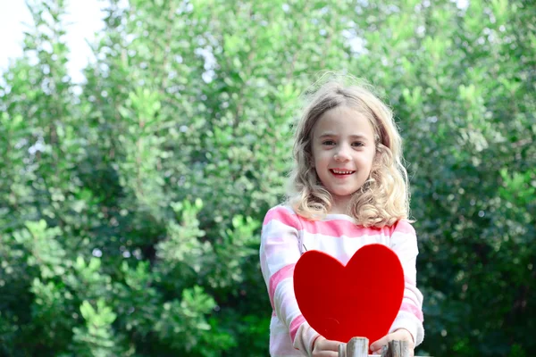 Prachtige blond meisje sittig o een vertakking van de beslissingsstructuur houden grote voelde hart in haar handen — Stockfoto