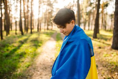 Genç bir adam kendini ormandaki Ukrayna bayrağına sardı. Bağımsızlık, bayrak, barış, savaş yok