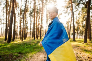 Genç bir adam kendini ormandaki Ukrayna bayrağına sardı. Bağımsızlık, bayrak, barış, savaş yok