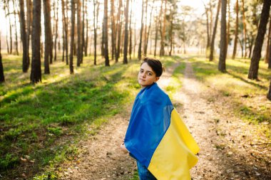 Ormanda sarı ve mavi bayrak taşıyan gülümseyen çocuk. Ukrayna 'yı seviyor, savaş kavramı yok. Güneşli bir günde Ukrayna bayrağı taşıyan genç adam