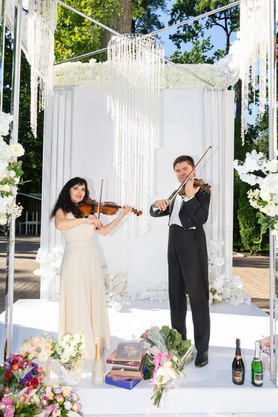Erkek ve kadın düğün kemerinin altında keman çalıyor..