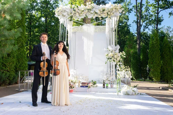 man and woman violinists on wedding arch background.