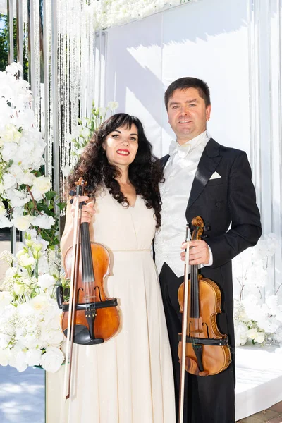 man and woman violinists on wedding arch background.