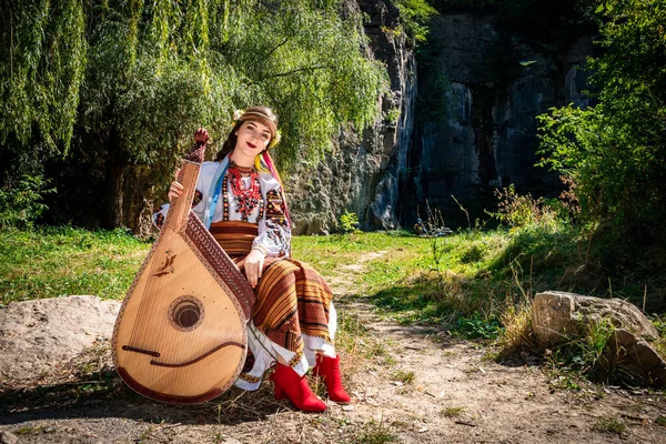 身着正宗民族服装的乌克兰音乐家坐在岩石旁边 乌克兰妇女在演奏民谣之前 带着管弦乐队乐器 — 图库照片