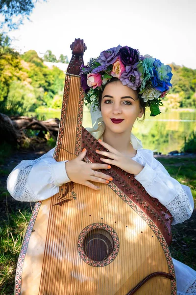 身穿民族服装 手持乌克兰民族弦乐乐器坐在河边的乌克兰年轻妇女 — 图库照片