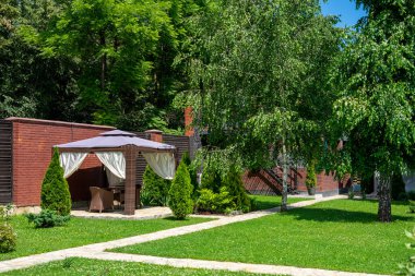 Yeşil çimenli bir arka bahçe ve yeşil ağaçların yanında bir çardak..