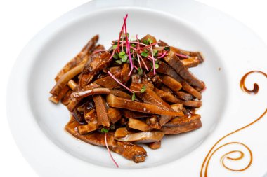 Fried pieces of pork in sauce decorated with microgreens. Marinated pig ears.