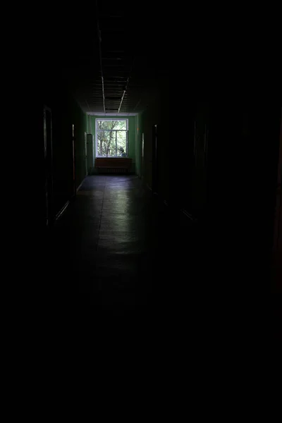 A window at the end of a dark, unlit corridor. Dark dark dark corridor of an abandoned building.