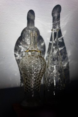 Two transparent vintage bottles and an abstract shadow from them on the wall.