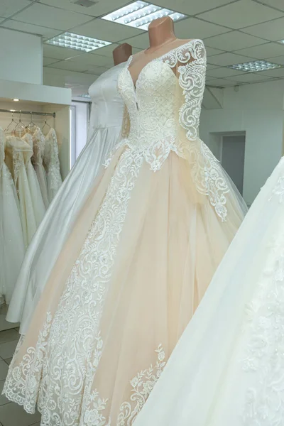 A beautiful cream wedding dress on a mannequin. A wedding dress on the background of other wedding dresses in a wedding salon.