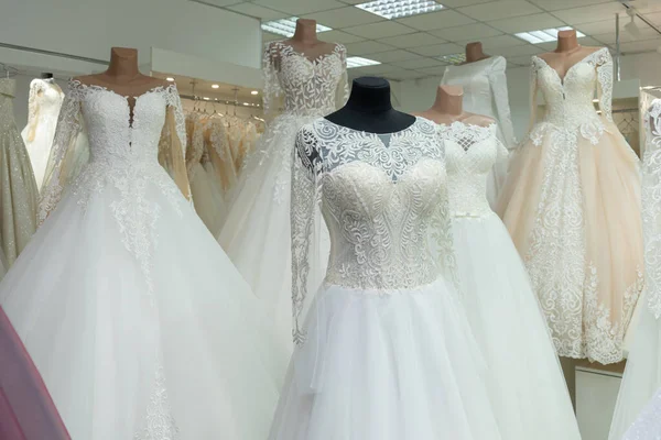 A close-up of a wedding dress against the background of other wedding dresses in a bridal salon.