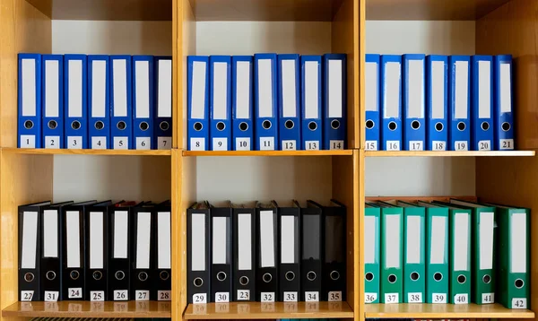 A bookshelf with many different folders on it. There are many different folders on the bookshelf at school.