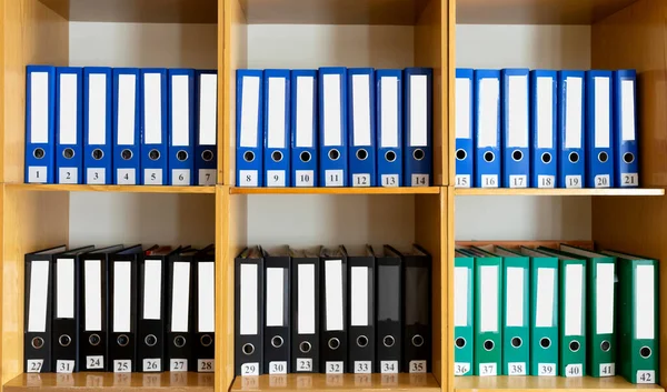 A bookshelf with many different folders on it. There are many different folders on the bookshelf at school.