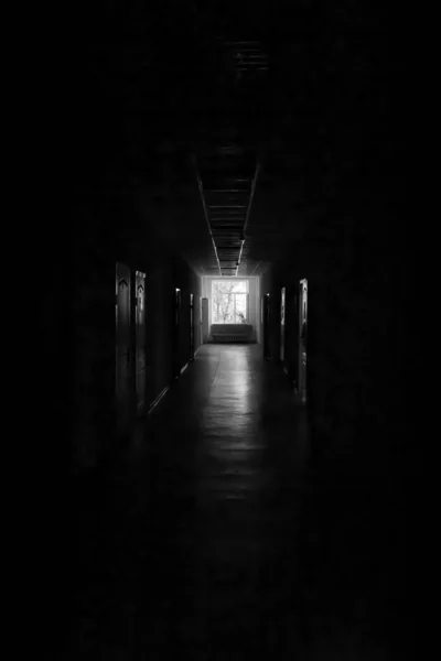 A window at the end of a dark, unlit corridor. Dark dark dark corridor of an abandoned building.