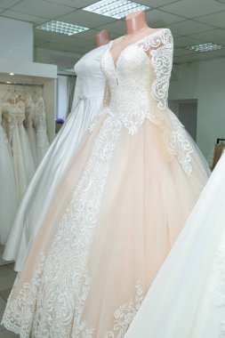 A beautiful cream wedding dress on a mannequin. A wedding dress on the background of other wedding dresses in a wedding salon.