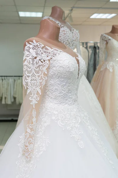 A beautiful white wedding dress on a mannequin. A close-up of a dress against other wedding dresses in a bridal shop.