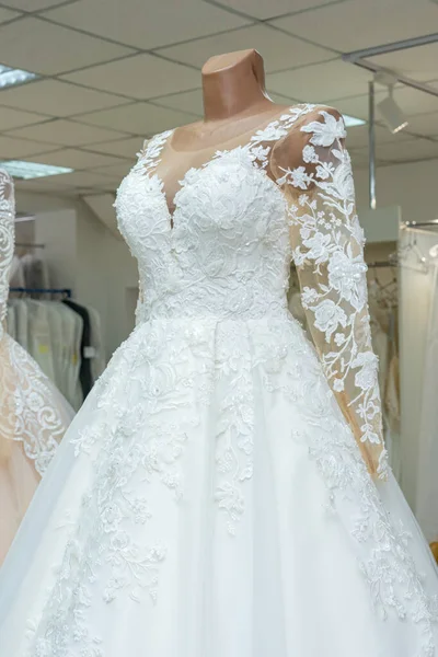 A beautiful white wedding dress on a mannequin. A close-up of a dress against other wedding dresses in a bridal shop.