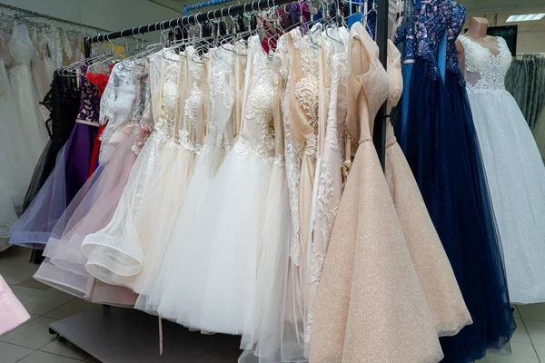 Many different evening dresses and bridal dresses on a hanger in the store.