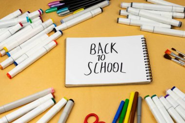 A variety of school supplies and a notebook in the center with the inscription back to school.