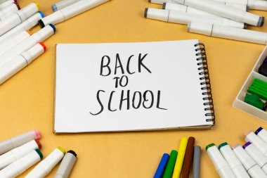 Back to school notebook and other supplies on yellow table.
