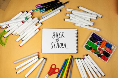 Many different office supplies. School markers, pens and plasticine. Inscription on notebook back to school.
