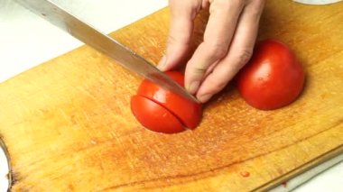 Chopping red tomatoes into pieces. The cook crumbles the tomato with a knife on a wooden plank. Close-up.
