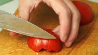 A woman cook cuts tomatoes on a wooden board. Close up