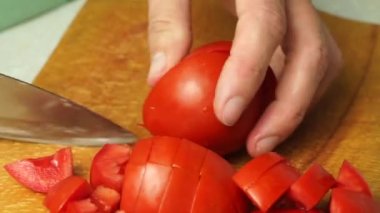 Chopping tomatoes with a knife on a wooden board.