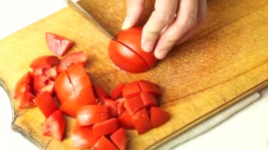 Chopping tomatoes by a woman cook on a kitchen board.